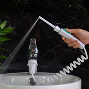Dental flosser in use at bathroom sink with water spray dispersing, hand holding white device with teal nozzle