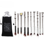 Full set of 10 gunmetal silver wand-shaped makeup brushes laid flat next to branded black velvet and silver organza pouch on white background