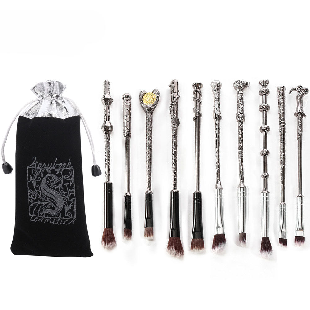 Full set of 10 gunmetal silver wand-shaped makeup brushes laid flat next to branded black velvet and silver organza pouch on white background