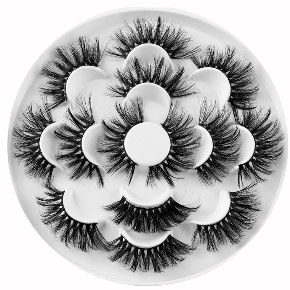 Overhead flat-lay of 7 pairs of false eyelashes arranged in a flower pattern on white storage tray
