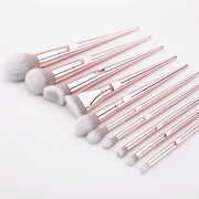 Full set of 10 rose gold makeup brushes with soft white-grey bristles fanned out on a white background