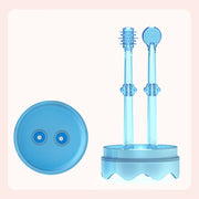 Two translucent blue silicone baby toothbrushes standing in a wavy-edge base holder, alongside a top-view of the circular lid with two holes