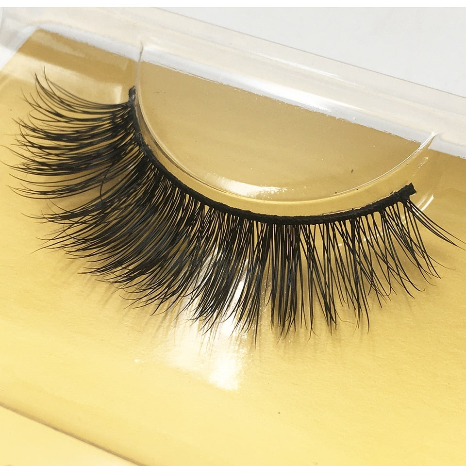 Close-up of dramatic mink false eyelashes on golden surface displaying full volume and feathered fiber detail