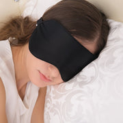 Woman wearing black silk sleep mask while resting on white pillow with relaxed expression