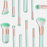 Flat lay of all 10 mint green and rose gold makeup brushes scattered artistically on a light grey background