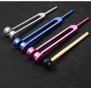 Five colorful 128 Hz tuning fork healing devices arranged in gradient showing available color options: silver, blue, pink, burgundy, and natural wood