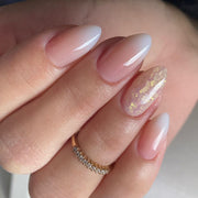 Manicured hand wearing gradient pink-to-white ombre press-on nails with gold glitter accent nail, gold ring visible