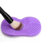 Purple silicone brush cleaning mat with a makeup brush being scrubbed across ridged texture zone