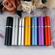 Seven 5ml aluminum perfume atomizers in black, silver, gold, blue, purple, and red arranged in a row against a floral background