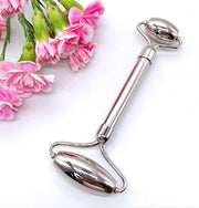 Stainless steel dual-roller massage stick displayed with pink carnations on white background