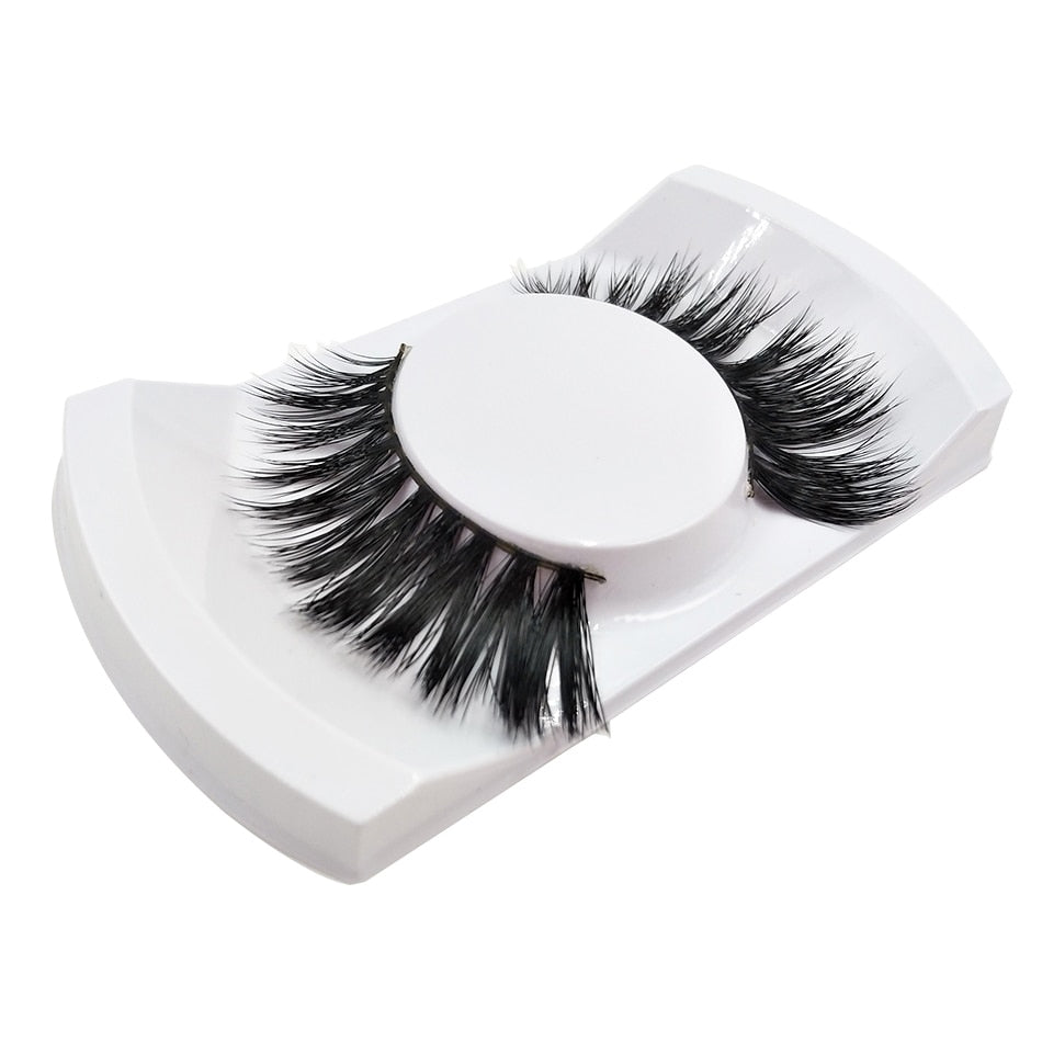 Pair of dramatic 3D wispy mink lashes on white curved plastic base at angled perspective