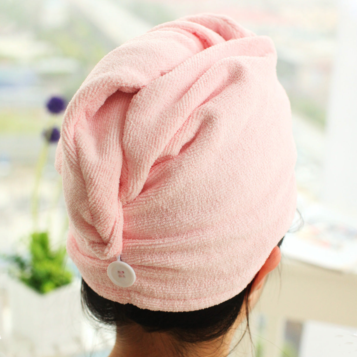 Woman wearing pink hair drying cap with turban-style wrap and button closure, styled at crown