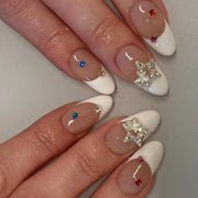 Close-up of hands wearing ornate French tip nails with 3D silver stars and multicolored rhinestone studs