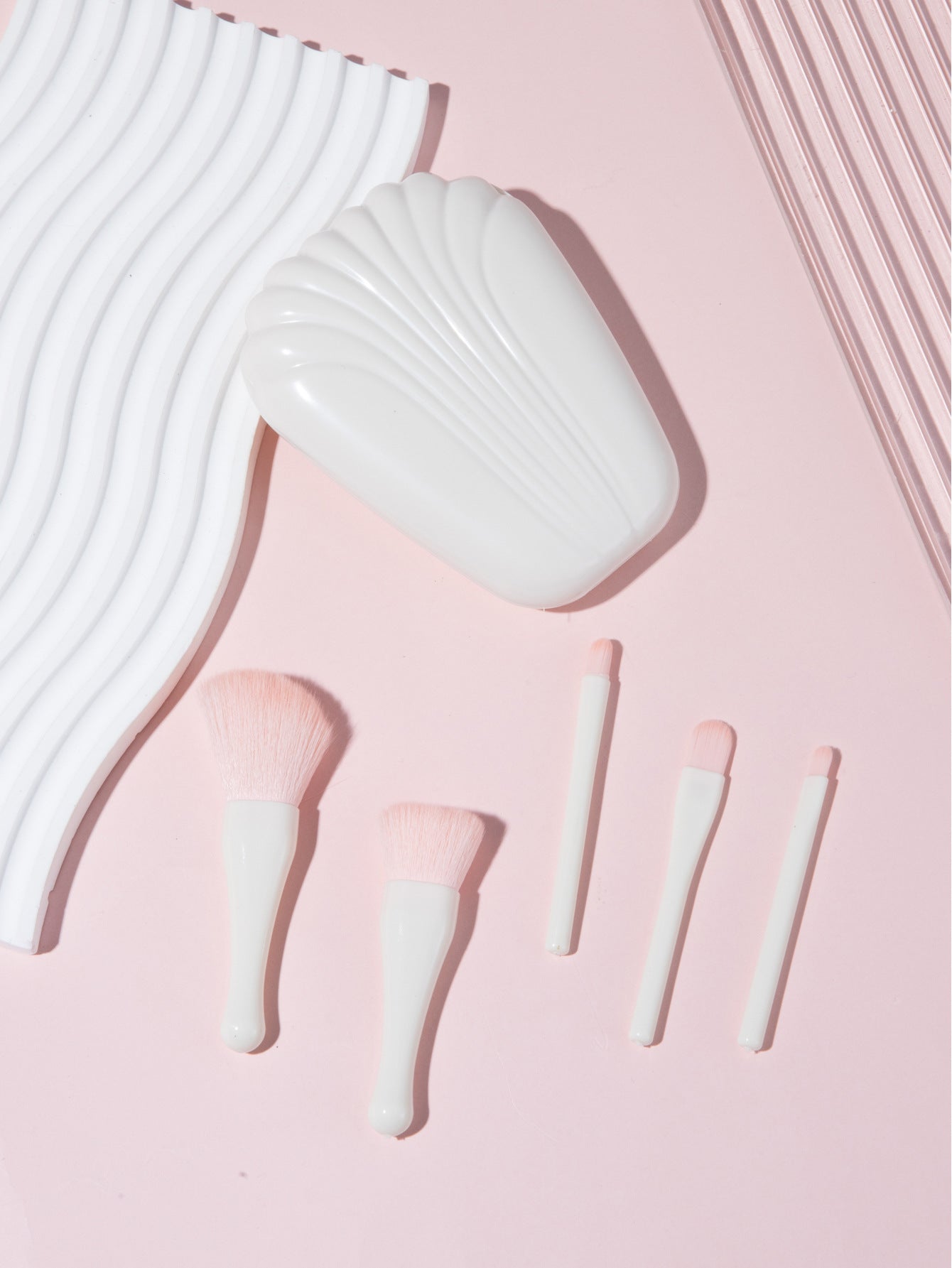 Complete 5-piece brush set with shell case arranged against pink backdrop with wavy white elements