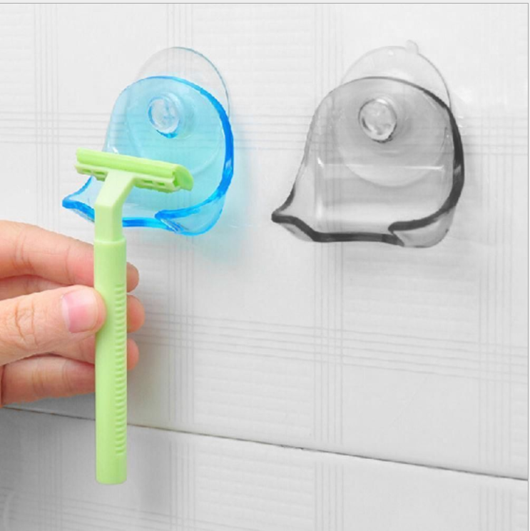 Hand inserting a green razor into a blue suction cup holder on a tiled wall, with a grey version mounted beside it