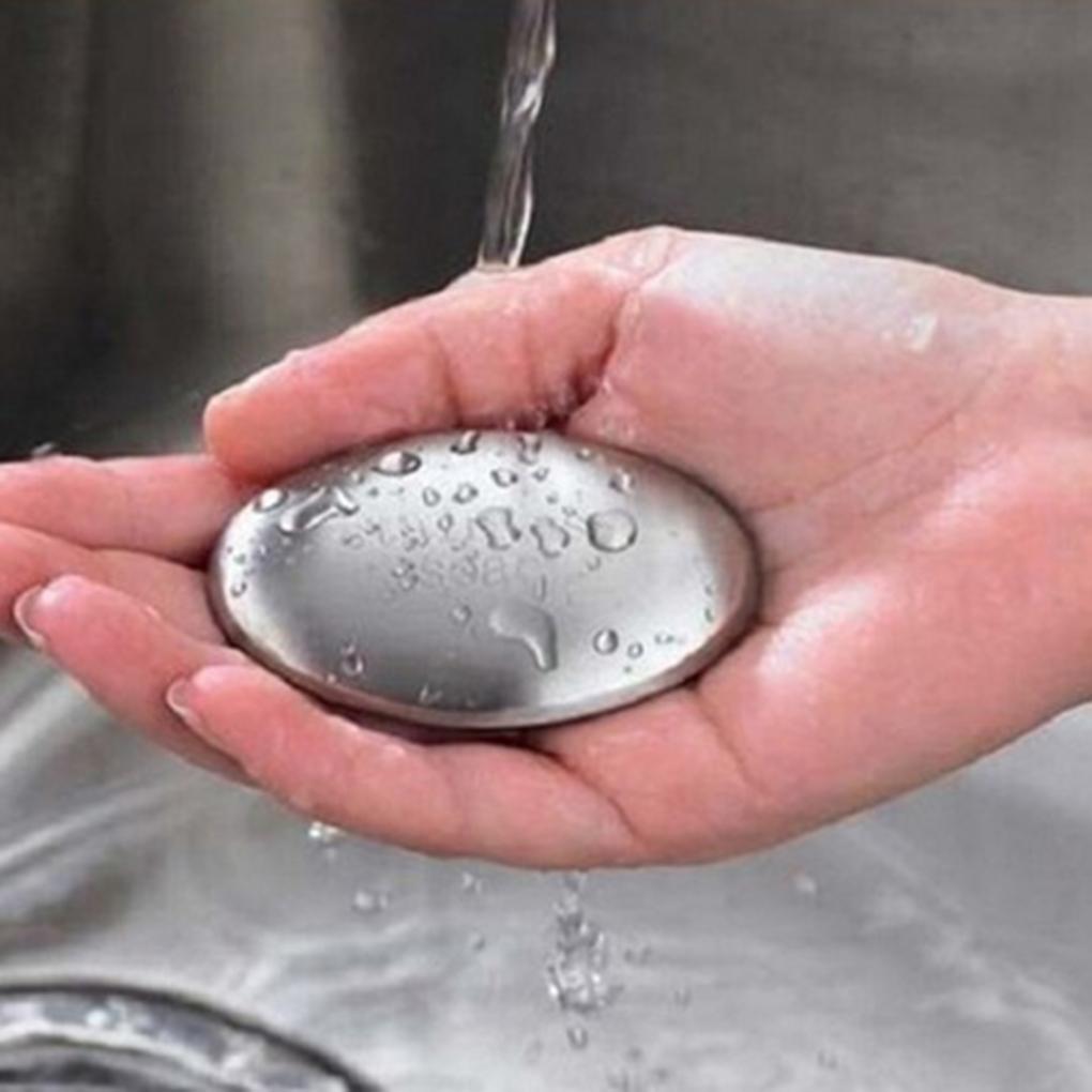 Hands holding stainless steel bar under running water with visible water droplets, demonstrating real-world kitchen use