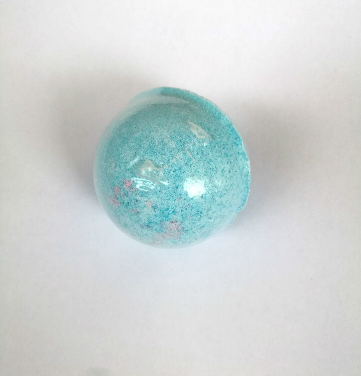 Close-up of a single teal blue bath bomb with pink speckles and glossy surface texture