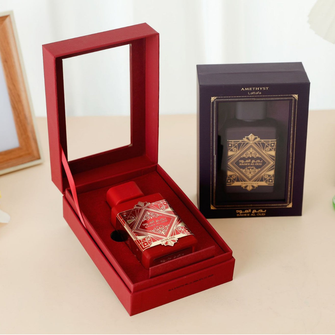 Bade'e Al Oud Sublime red bottle in open velvet-lined clamshell gift box beside Amethyst navy edition box on a beige surface