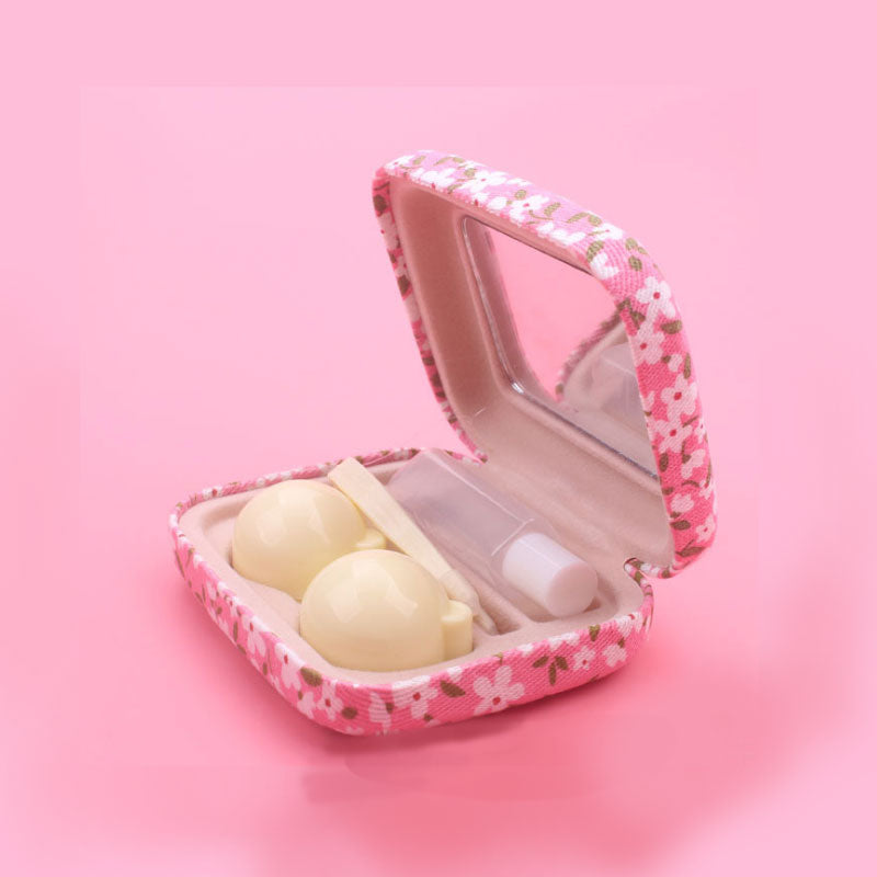 Open pink floral case on pink background displaying two cream-colored false eyelashes, white applicator tool, and built-in mirror