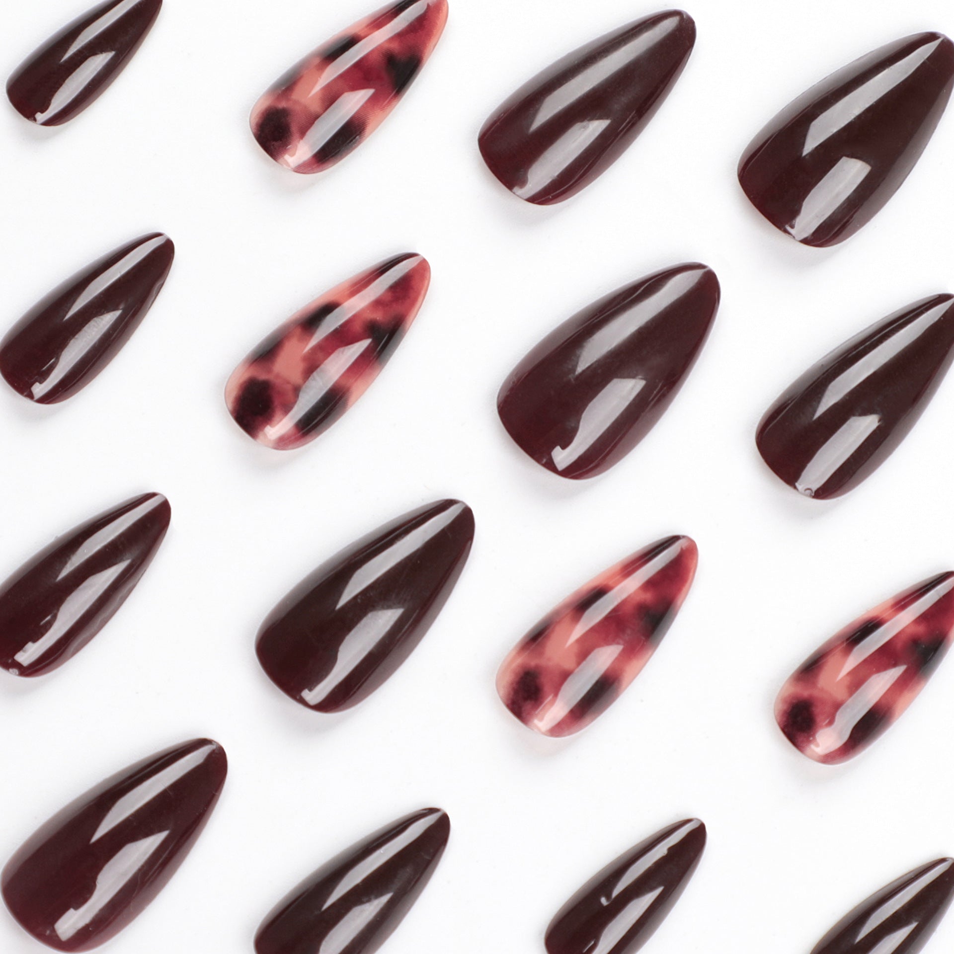 Close-up scattered arrangement of almond nails highlighting the deep burgundy solid nails and intricate rose-black tortoiseshell patterned nails