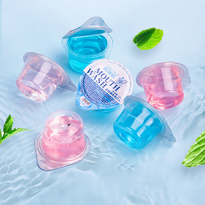 Styled flat lay on light blue water-textured background with fresh mint leaves, showing multiple pods in use with clear liquid visible inside translucent capsules