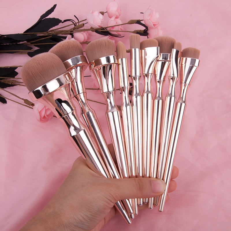 Close-up of multiple brushes including a large oval foundation brush with brown bristles on a pink floral backdrop