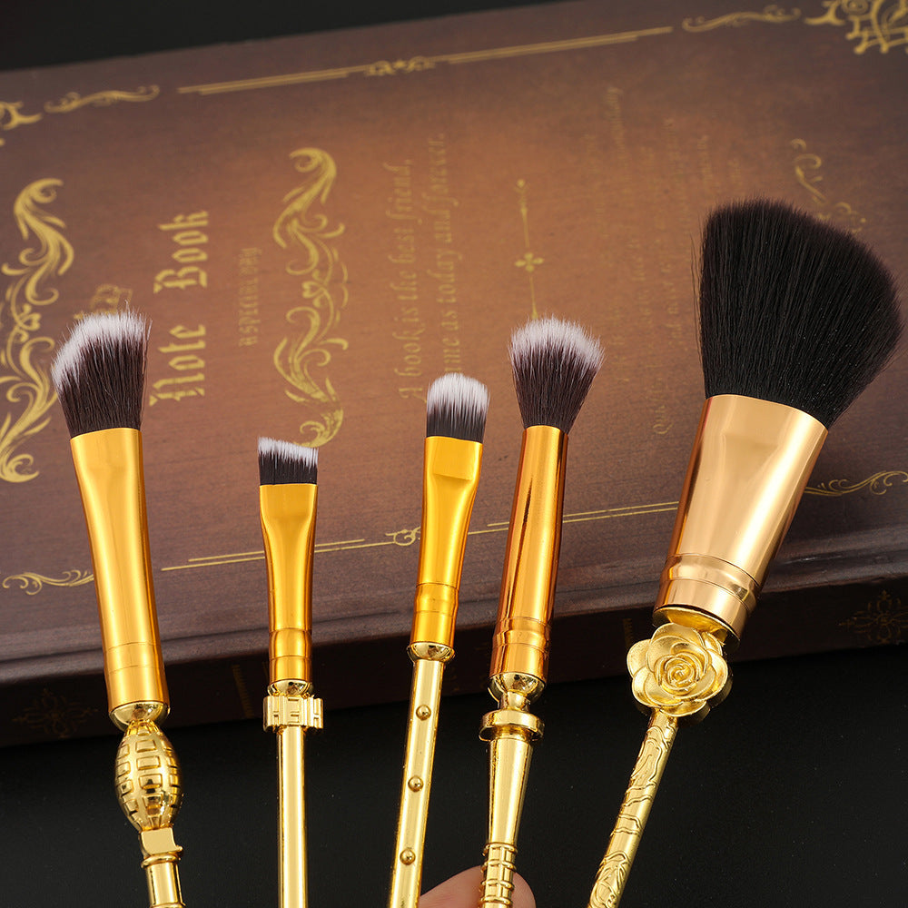 Close-up of brush heads showing varied sizes from large powder fan to small liner brush with gold ferrules and rose accent