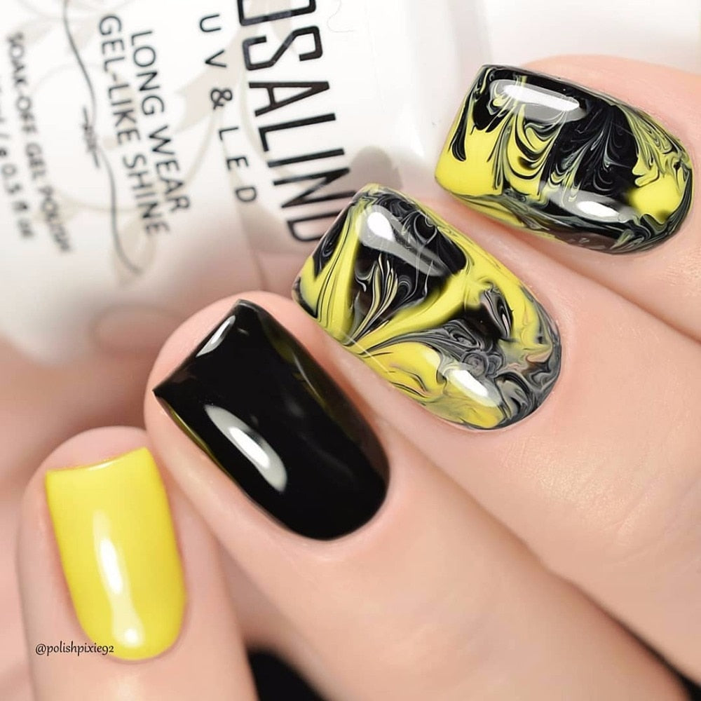 Real manicure on hands showing creative nail art with yellow, black swirl design and solid colors
