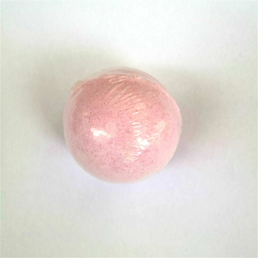 Pink bath bomb individually wrapped in clear plastic shrink film on white background