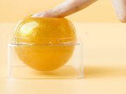 Close-up of hands holding transparent gel sphere with rotating band closure, showing crystal-clear golden formulation